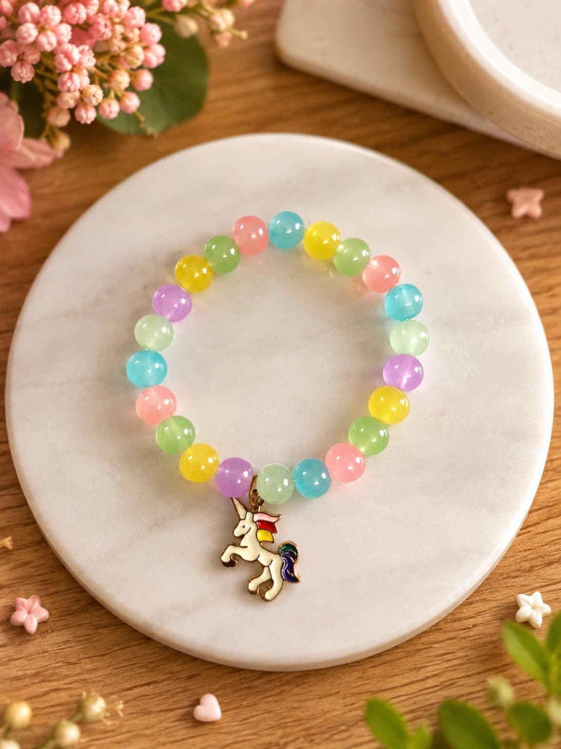 Handmade pastel rainbow jelly bead stretch bracelet with a unicorn charm on a marble plate